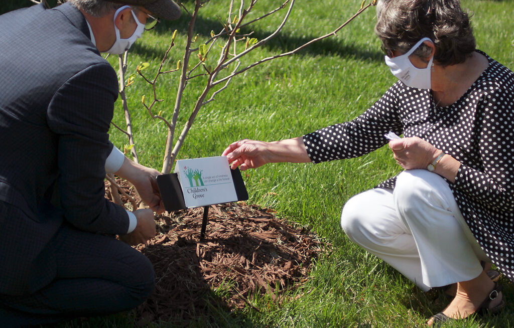 Peter Stiepleman, left, and Children's Grove founder Anne Deaton unveil the dedication plaque placed at the base of the magnolia tree